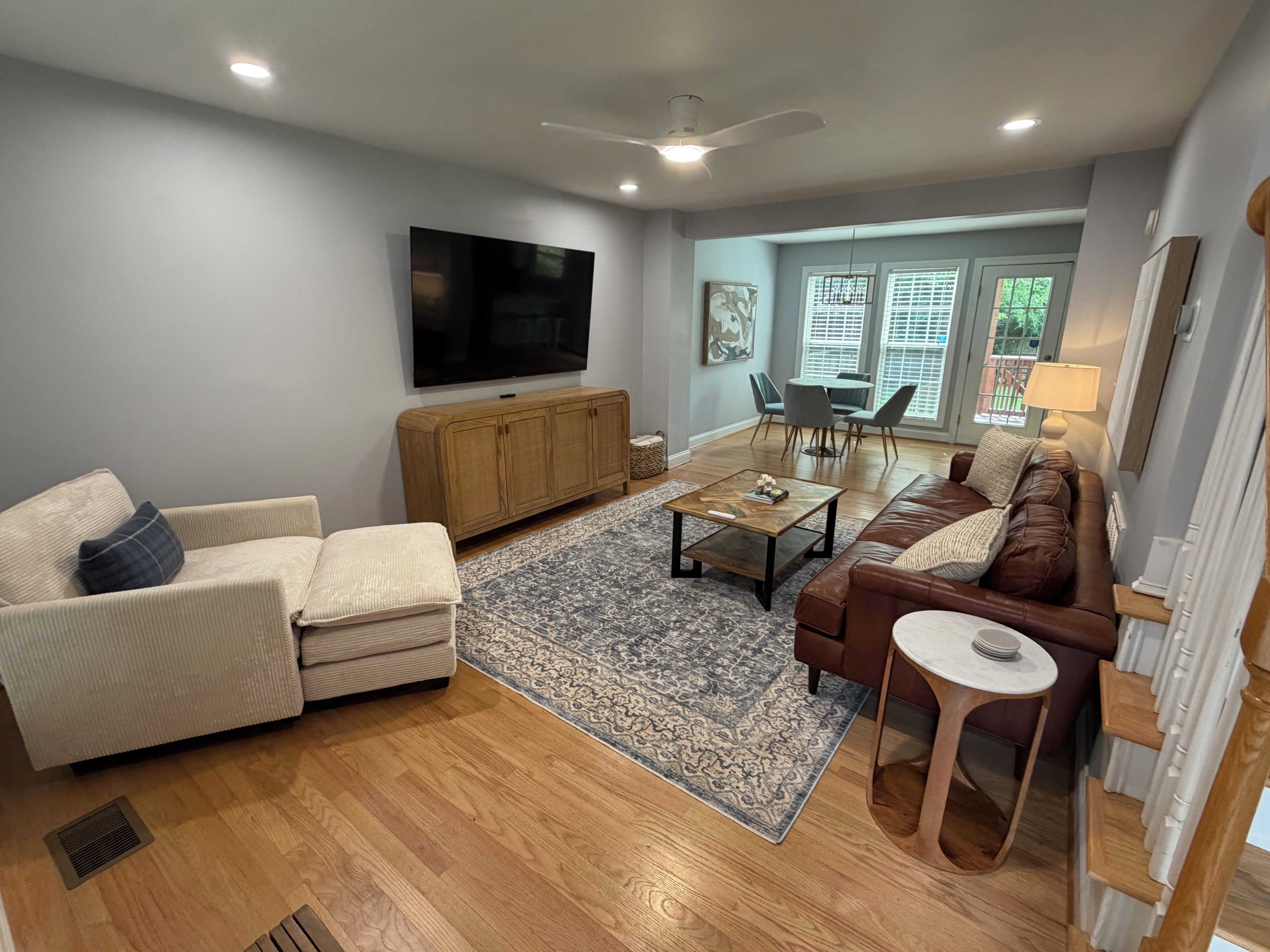 A living room with a sofa, armchair, coffee table, and a television mounted on the wall.
