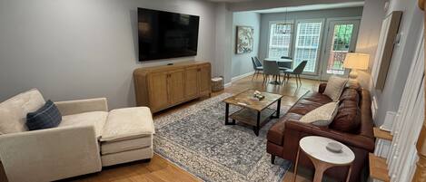 A living room with a sofa, armchair, coffee table, and a television mounted on the wall.