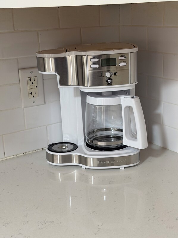 A Hamilton Beach coffee maker with a clear glass carafe and a digital display, placed on a white countertop.