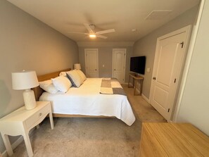 A bedroom with a bed, nightstand, lamp, ceiling fan, TV, and two doors.