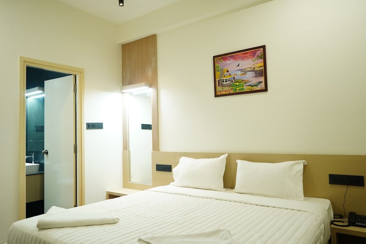 A hotel room with a bed, bedside table, nightstand, and a painting on the wall.