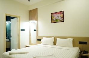 A hotel room with a bed, bedside table, nightstand, and a painting on the wall. - Kristal Grand (Bengaluru)