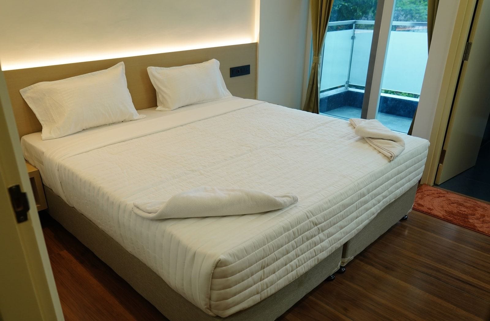 A hotel room with a large bed, a headboard, and a view of the outdoors through a sliding door.