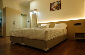 A bedroom with a bed, a bedside table, a nightstand, a wall-mounted light, and a painting. - Kristal Grand (Bengaluru)