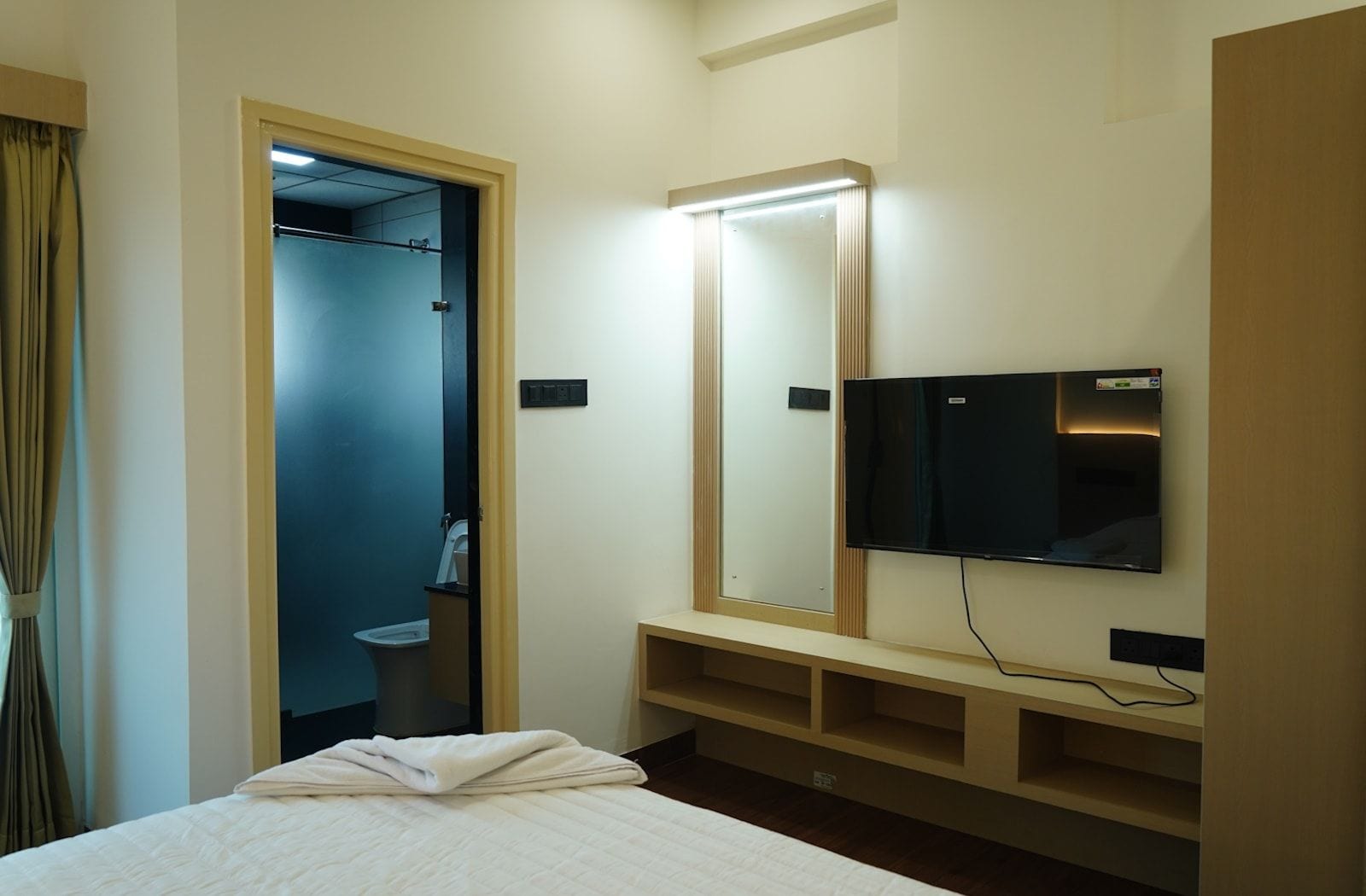 A hotel room with a bed, a television, a mirror, and a bathroom visible through an open door.