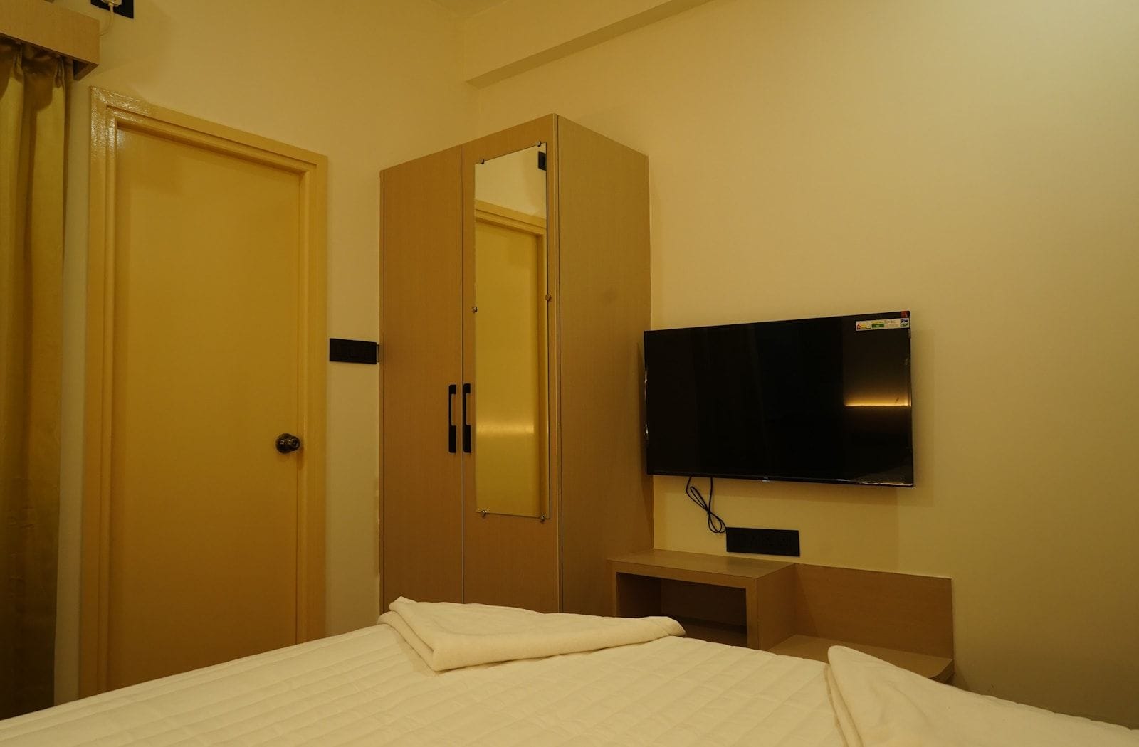 A hotel room with a bed, a wardrobe, a television, and a mirror.