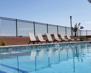 A swimming pool with a black metal fence, lounge chairs, and a clear sky.
