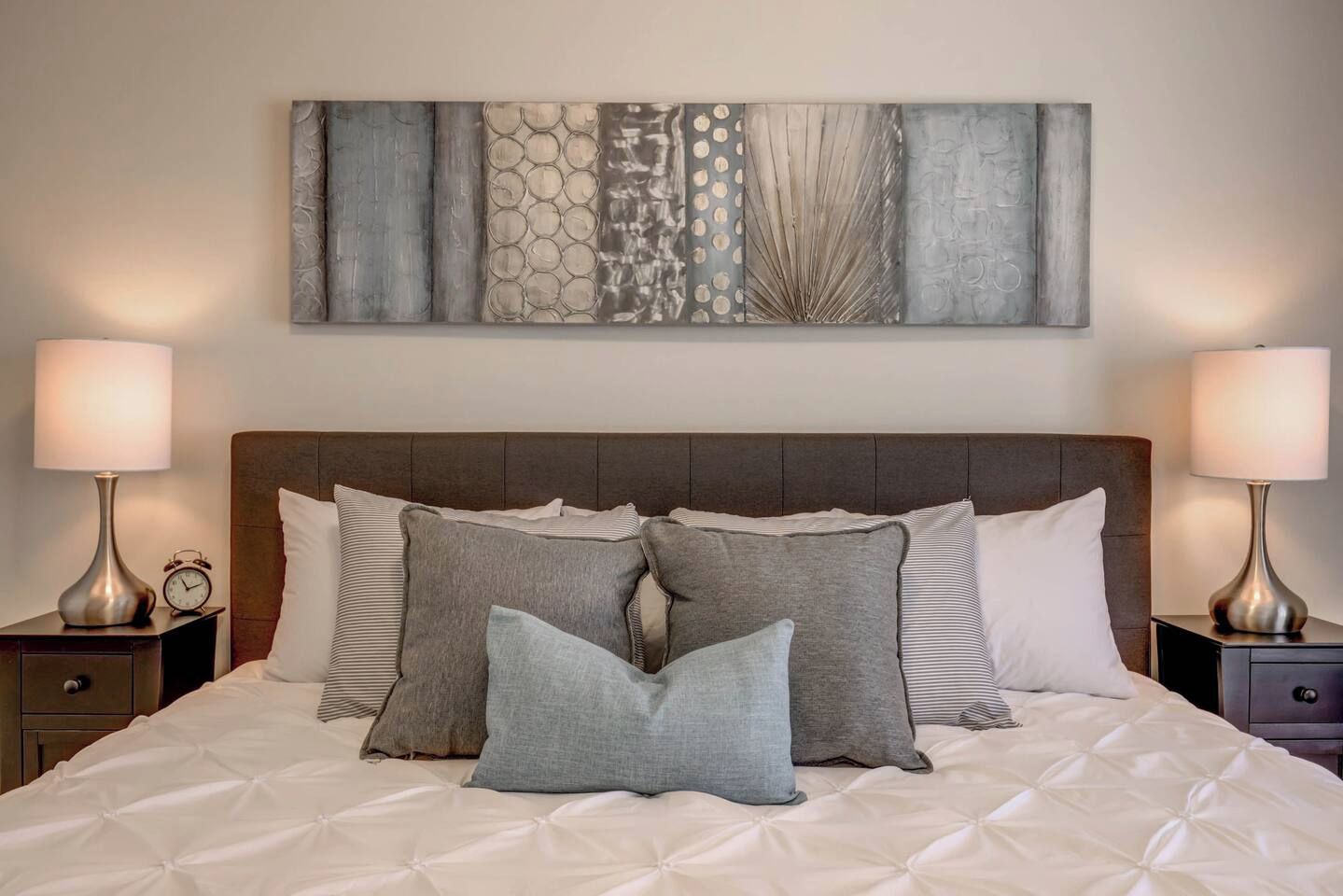 A neatly made bed with a tufted headboard, two bedside tables with lamps, and a large abstract artwork above the bed.