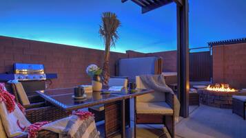 An outdoor patio with a grill, seating, and a fire pit.