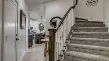 A staircase with a wooden handrail and carpeted steps leading to a kitchen area with white cabinets and a round mirror on the wall.