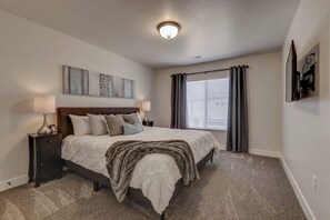 A bedroom with a bed, nightstands, a wall-mounted TV, and a window with curtains.