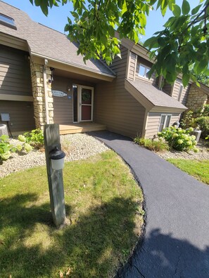 A building with a stone facade, a welcome sign, a door, and a paved walkway. - Fairway Stay: Golf Views, Pool & Near Eagle Ridge (Galena)