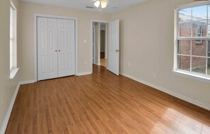 Une pièce dotée d’un plancher en bois, de portes blanches et d’une fenêtre donnant sur un bâtiment en briques.