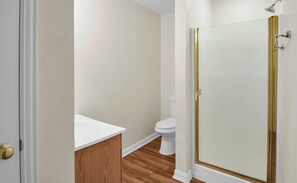 Ein Badezimmer mit Toilette, Holzwaschtisch und einer Duschkabine aus Glas.