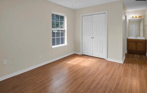 Une pièce dotée d’un parquet, d’une porte blanche, d’une fenêtre et d’une coiffeuse avec un miroir.