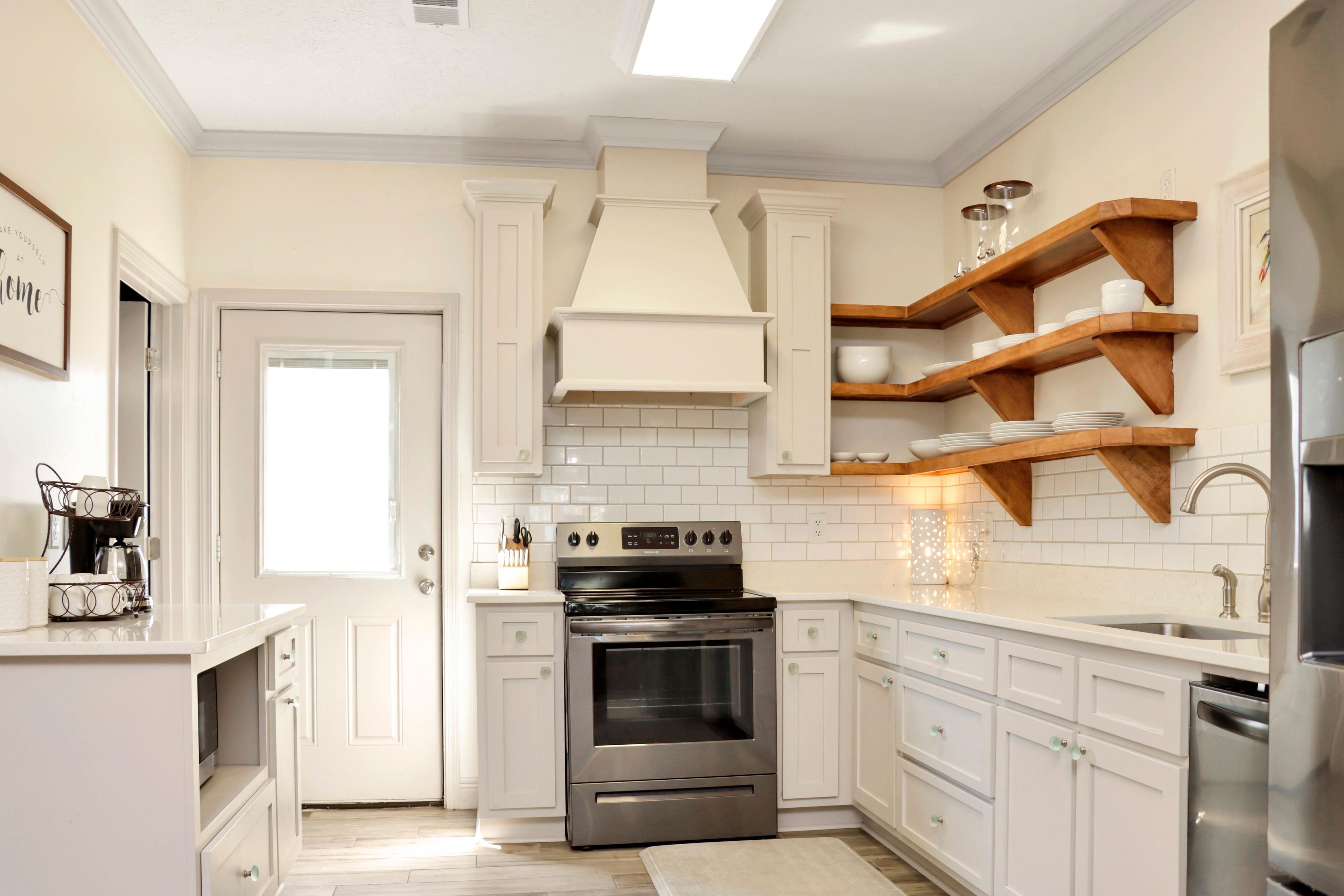 A modern kitchen with white cabinetry, a stainless steel oven, and wooden shelves above the countertop.