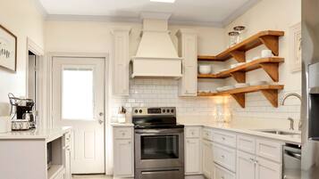 A modern kitchen with white cabinetry, a stainless steel oven, and wooden shelves above the countertop.
