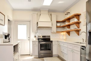 A modern kitchen with white cabinetry, a stainless steel oven, and wooden shelves above the countertop.