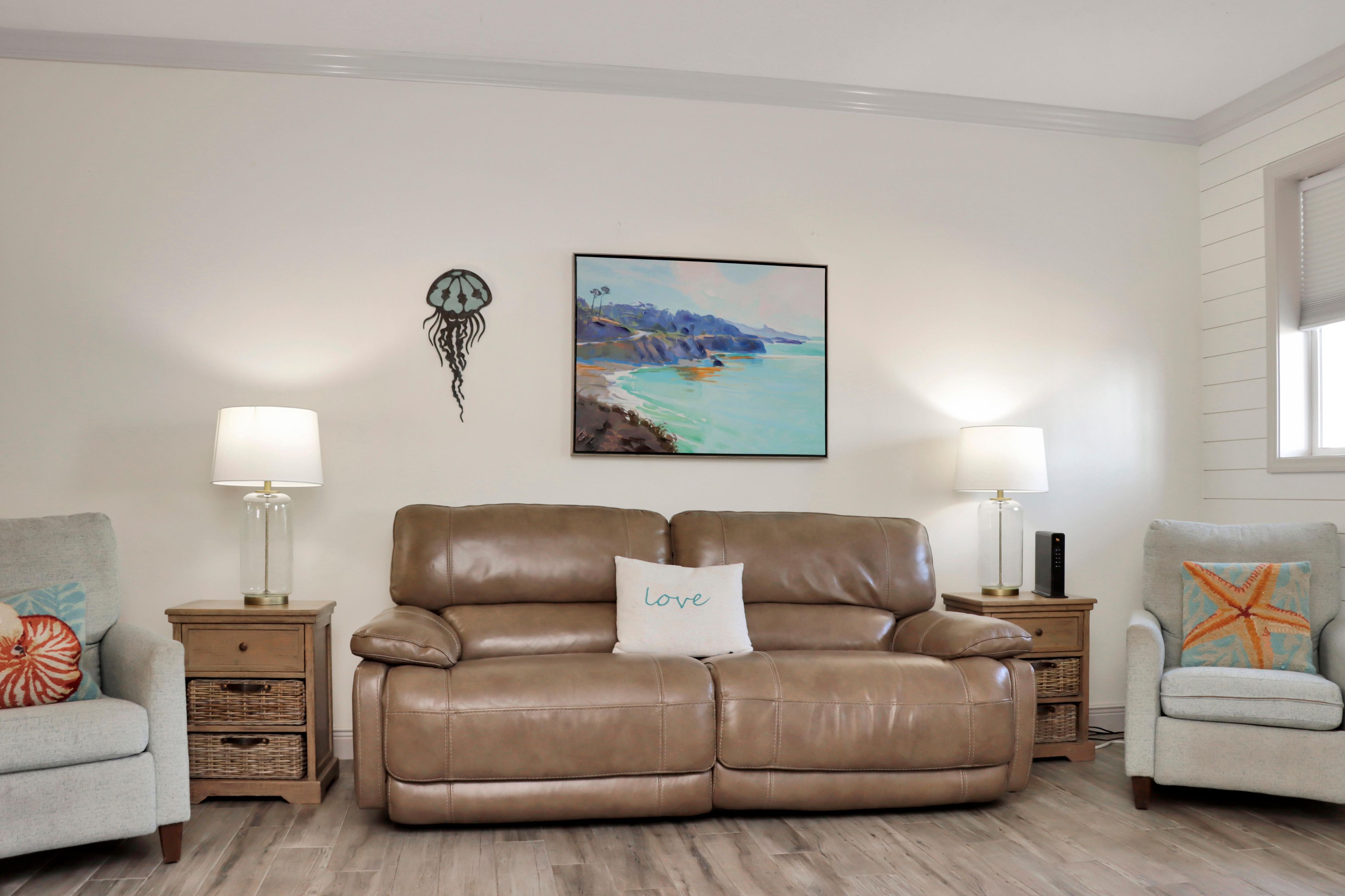 A living room with a brown leather sofa, two side tables with lamps, a wall-mounted painting, and a decorative starfish pillow.