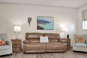 A living room with a brown leather sofa, two side tables with lamps, a wall-mounted painting, and a decorative starfish pillow.
