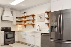 A modern kitchen with white cabinetry, a stainless steel refrigerator, and wooden shelves above the countertop. - Mystic Nights By The Sea (Port St. Joe)