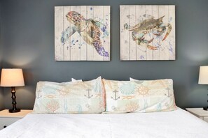 Un dormitorio con una cama, dos cuadros en la pared de criaturas marinas y una mesita de noche con lámpara.