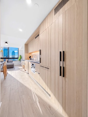 Een moderne keuken met houten kastjes, een inbouwoven en een raam met uitzicht op een stadsgezicht.