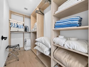 Een hotelkamer met een houten vloer, een bed met wit beddengoed, een zithoek met een stoel, en een kast met netjes opgevouwen handdoeken en een waterkoker.