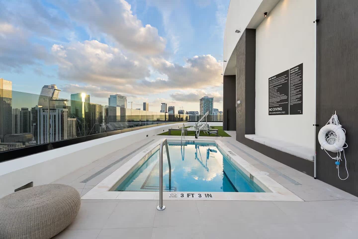 A rooftop pool with a city skyline view, a lifebuoy, and a sign indicating a 3 ft 3 in depth.