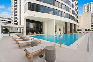 Een modern hotel met een zwembad op het dak, ligbedden en uitzicht op de stad.