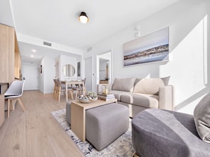 A modern living room with a sofa, ottoman, and a dining area with a table and chairs. - Luxury Worldcenter Condo - Pool - Gym - Parking (Miami)