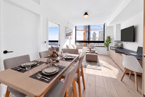 A modern dining area with a view of the city skyline, a flat-screen TV, and a dining table set for four. - Luxury Worldcenter Condo - Pool - Gym - Parking (Miami)