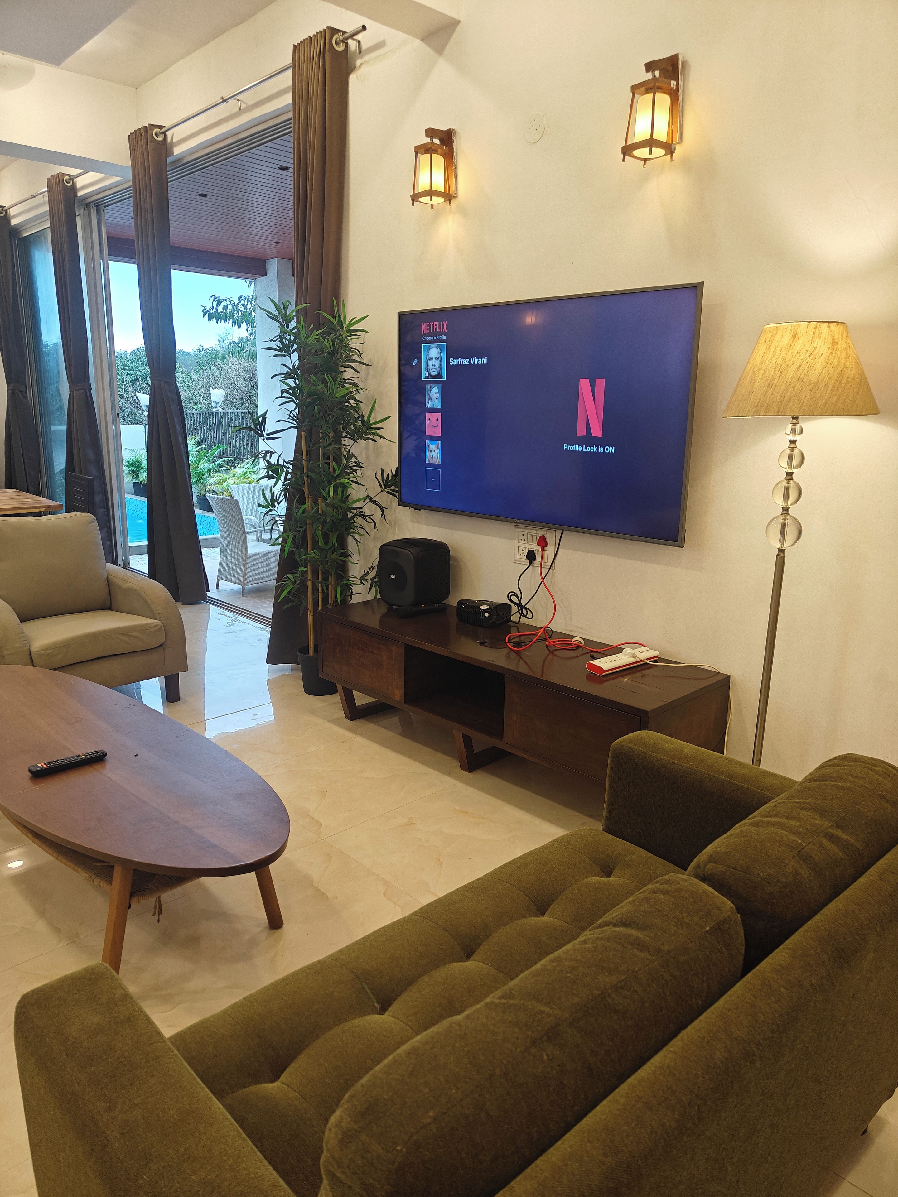 A living room with a flat-screen TV displaying a Netflix profile, a sofa, a coffee table, a lamp, and a speaker.