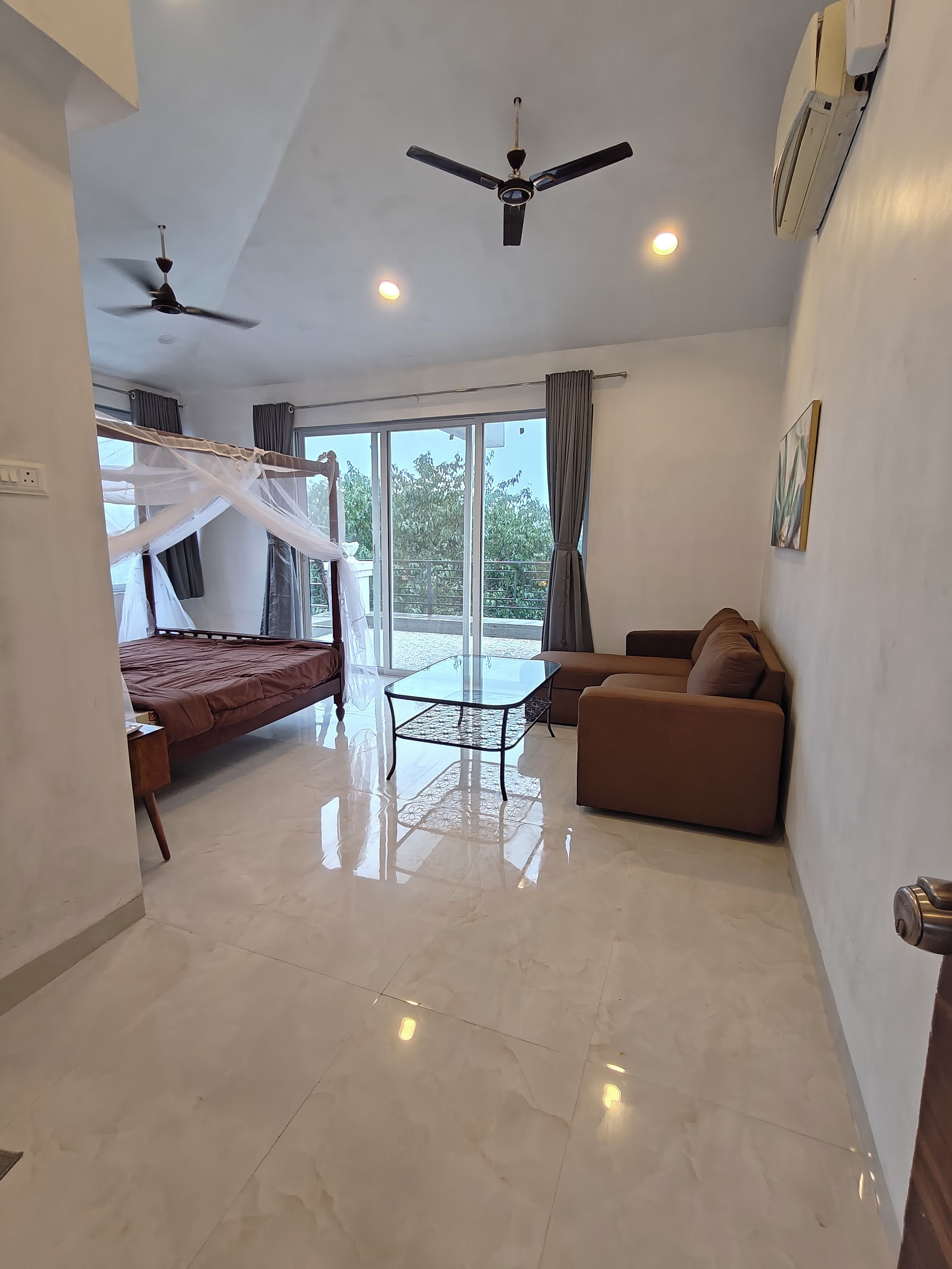 A modern bedroom with a bed, a glass table, a sofa, and a ceiling fan.