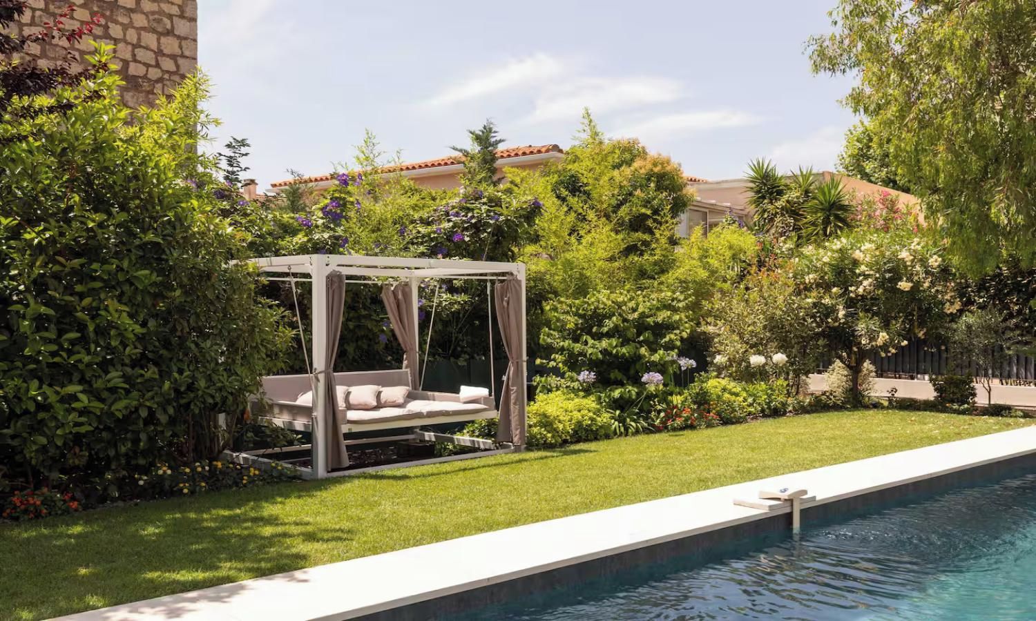 A garden with a pool, a swing bed, and lush greenery.