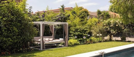 A garden with a pool, a swing bed, and lush greenery.