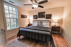 Ein Schlafzimmer mit einem Bett, einem Deckenventilator, einem Fenster und gerahmten Bildern an der Wand.