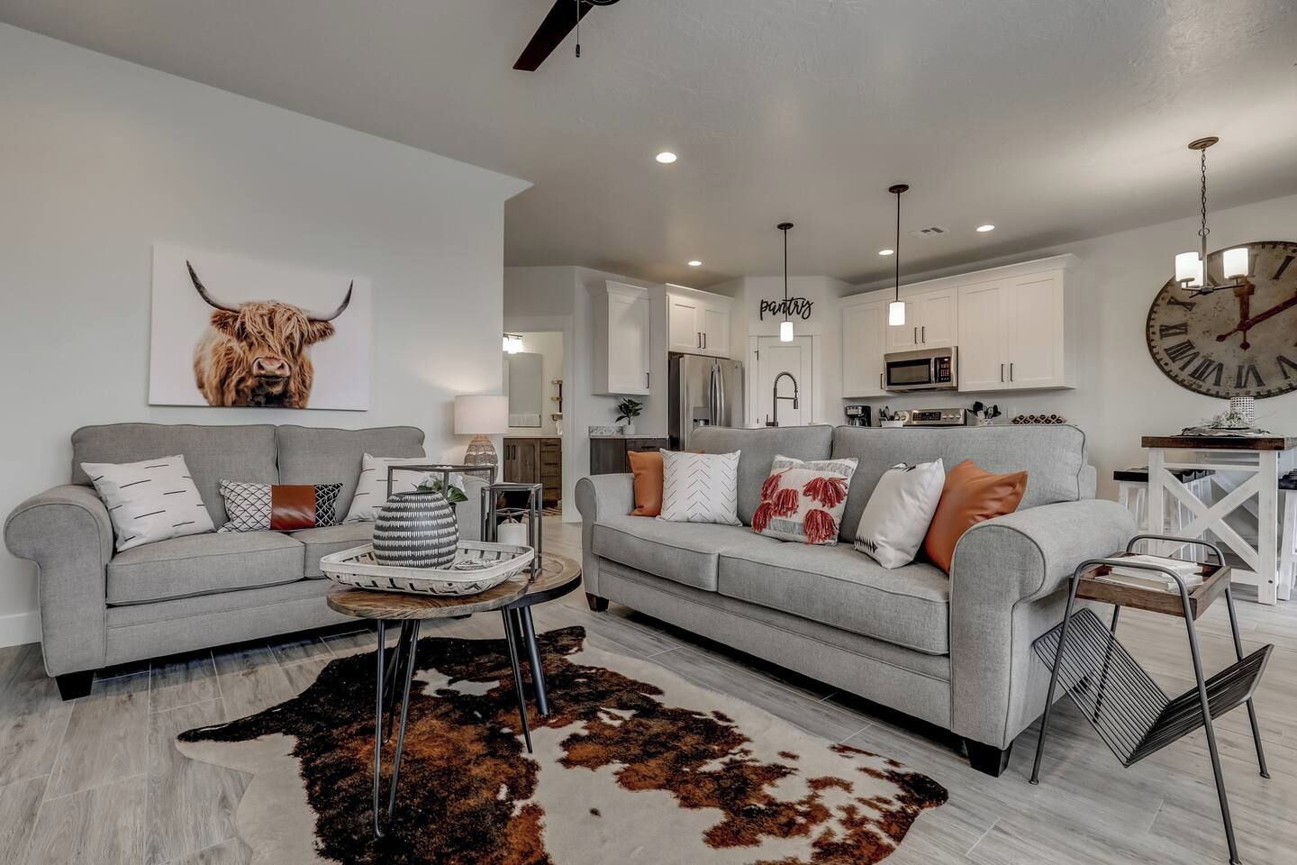 A modern living room with two grey sofas, a cowhide rug, and a large clock on the wall.