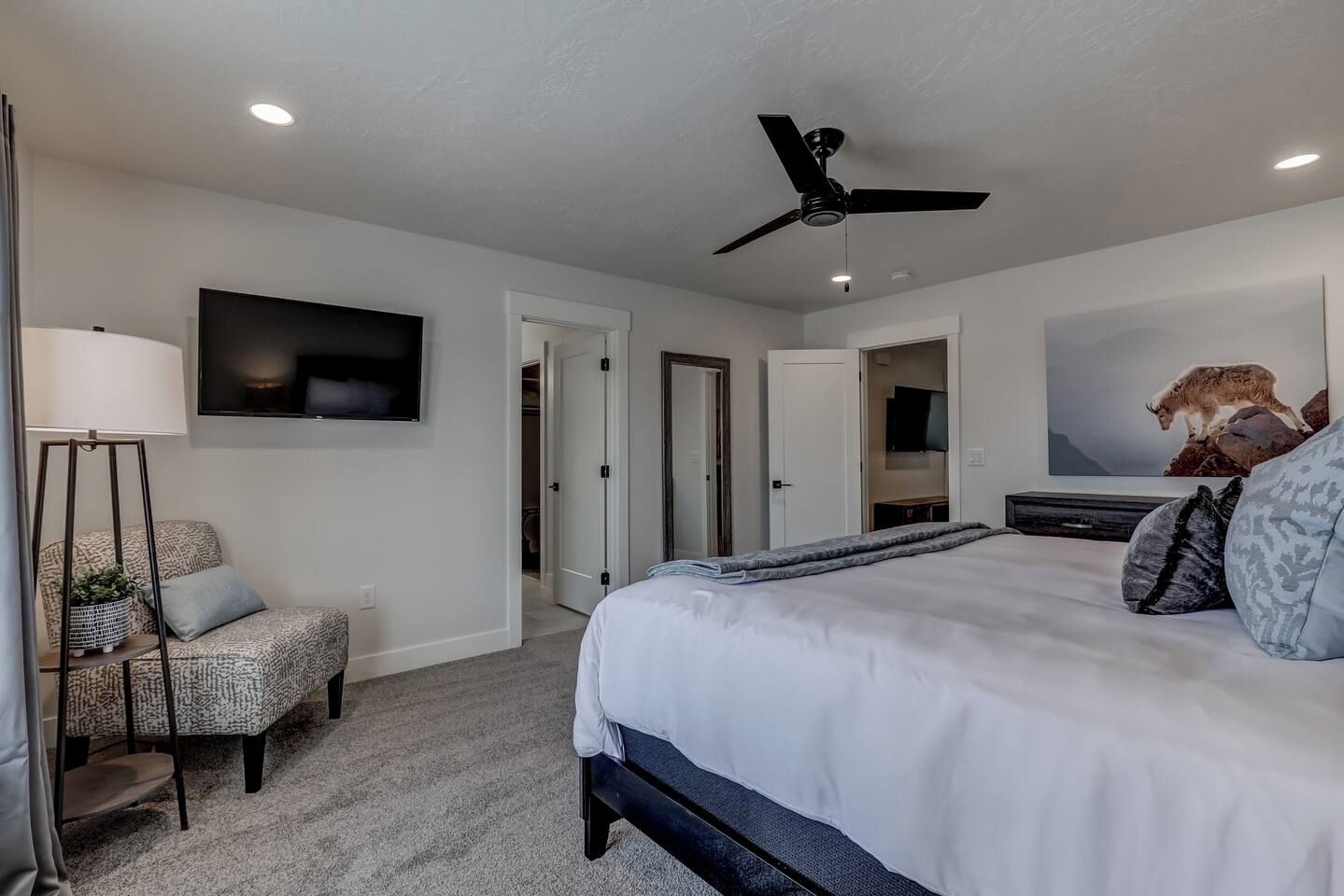 Un dormitorio moderno con una cama grande, un ventilador de techo, un televisor de pantalla plana y un cuadro de un paisaje montañoso.