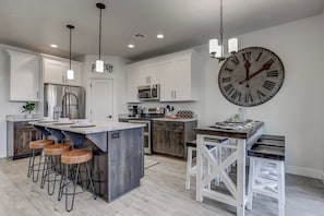 Een moderne keuken met een centraal eiland, barkrukken, roestvrijstalen apparatuur en een grote wandklok.