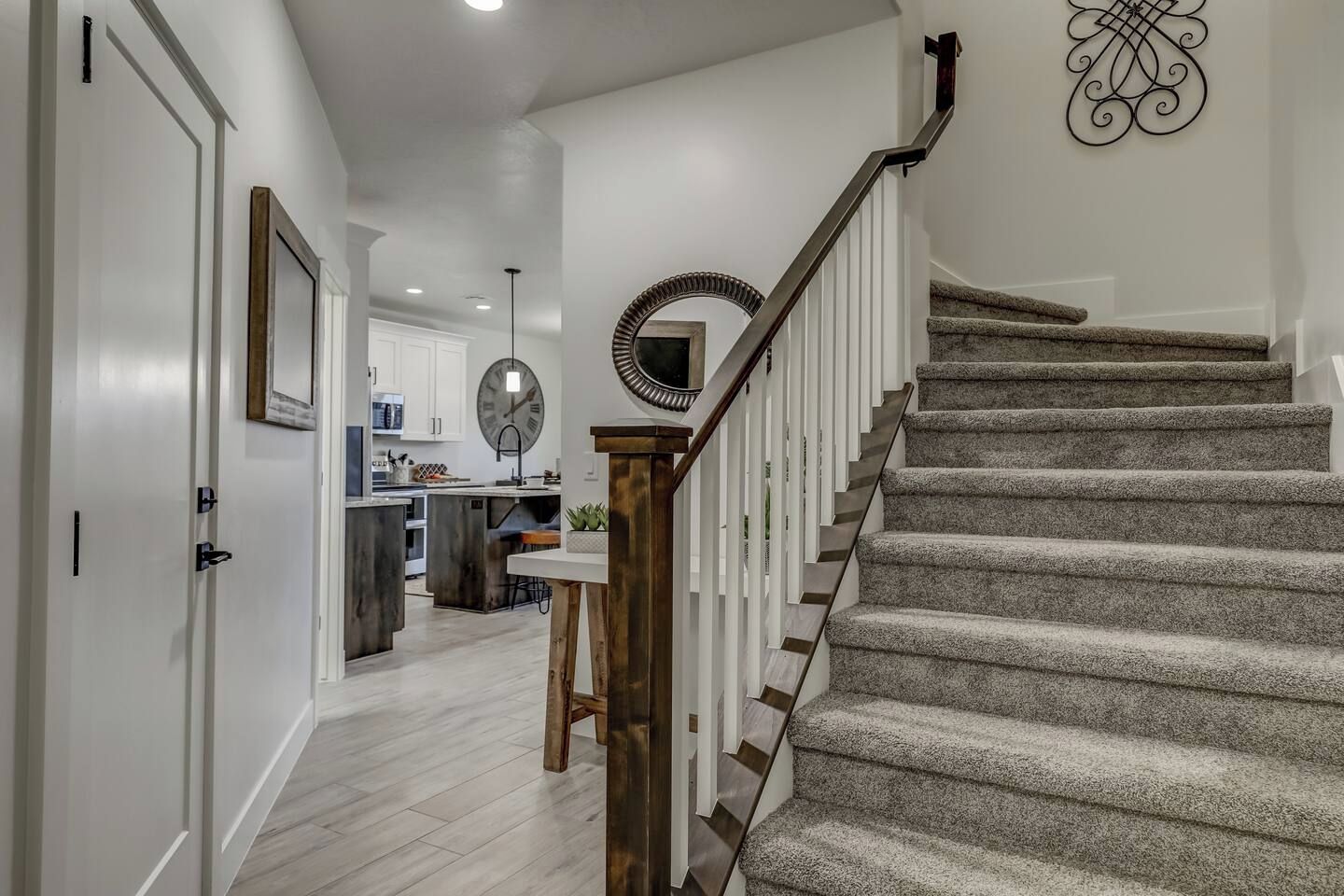 A staircase with a wooden handrail and carpeted steps leading to a kitchen area with white cabinets and a round mirror on the wall.
