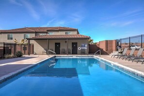 Une piscine avec un poste de surveillance pour les sauveteurs, des chaises longues et un bâtiment doté d’un toit en tuiles.