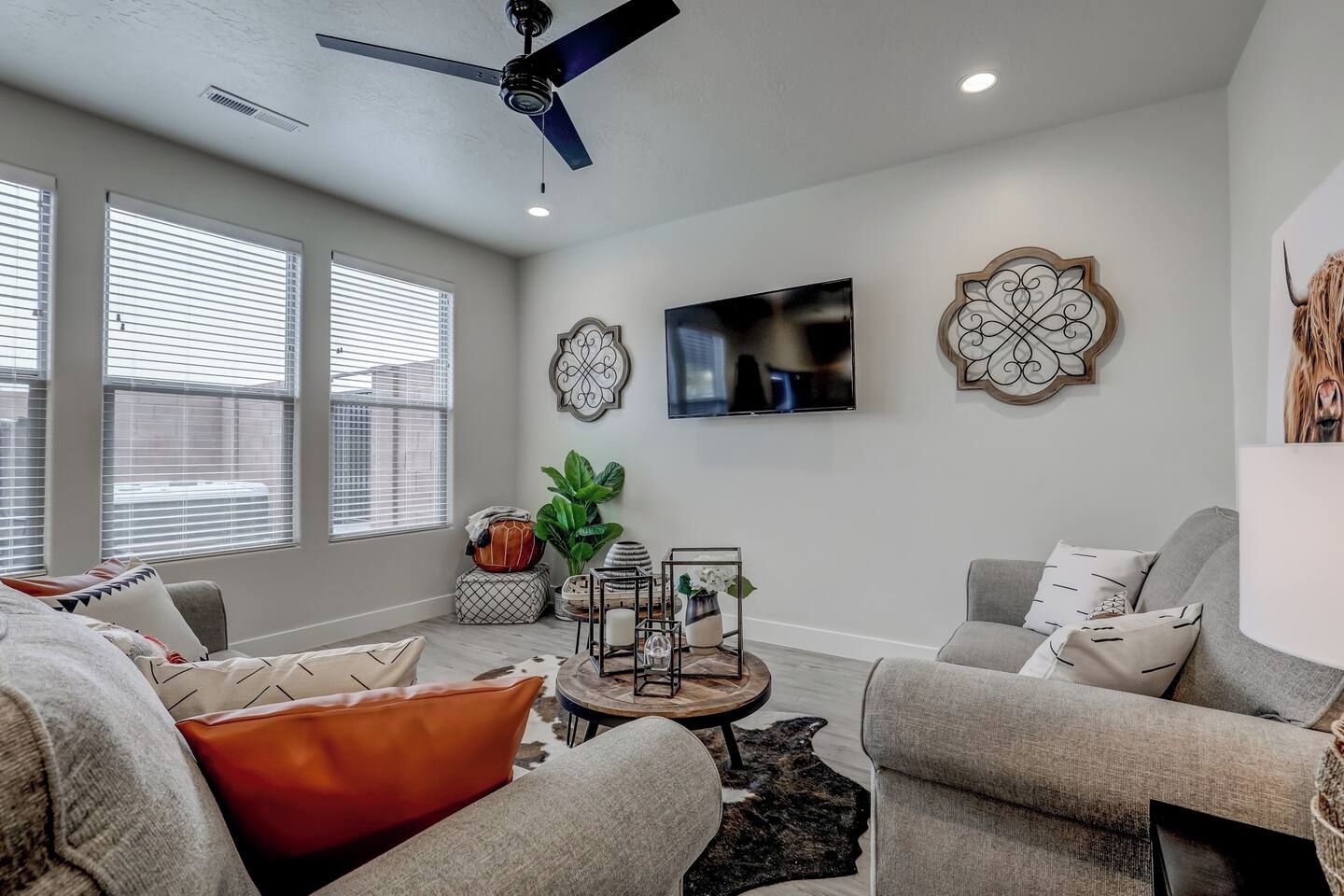A modern living room with a ceiling fan, a flat-screen TV, and decorative wall art.