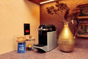 Una macchina per caffè, un contenitore di zucchero biologico, un boccale di metallo e uno sgabello di legno su un piano di lavoro in cucina.