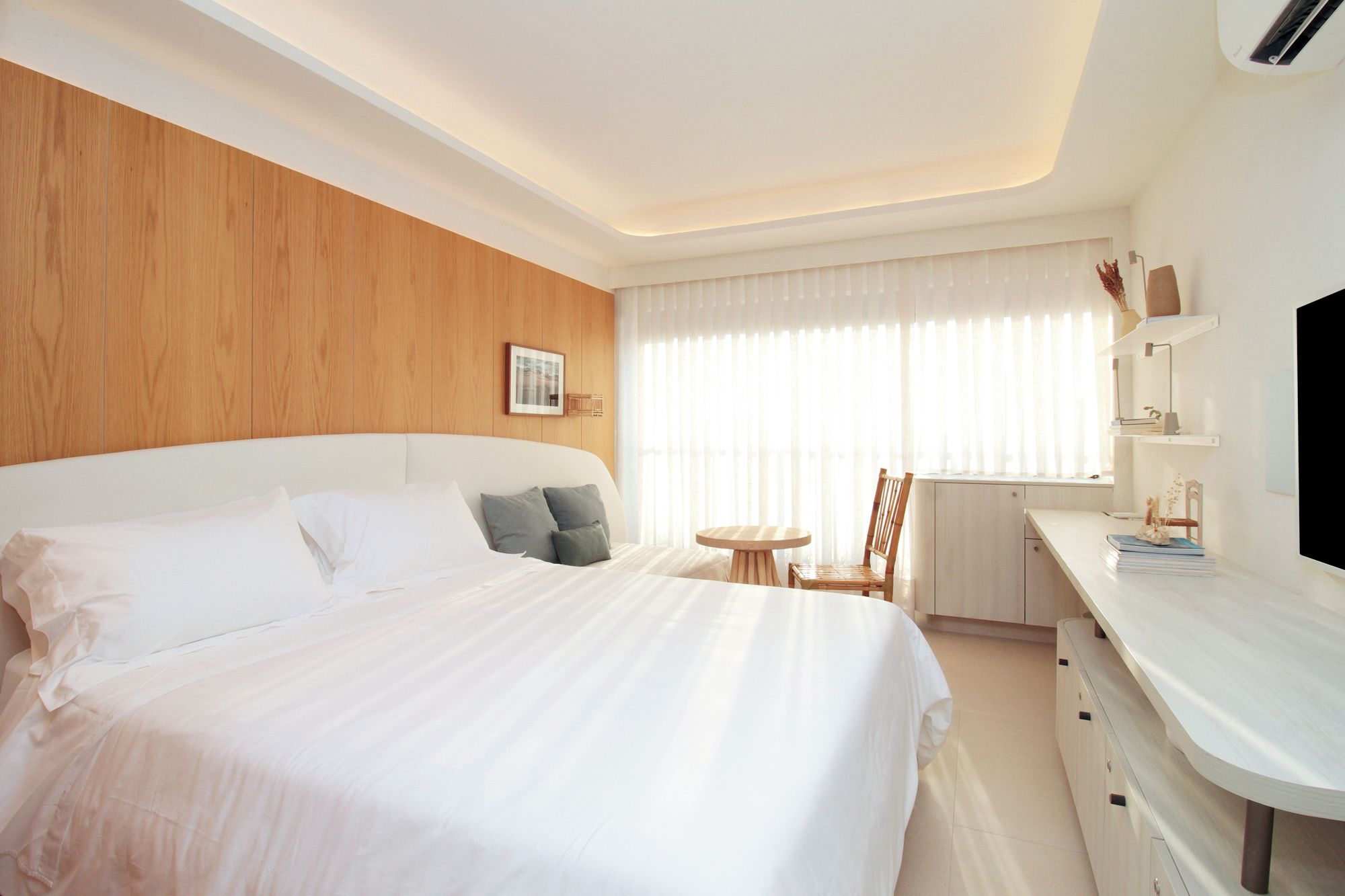 A hotel room with a large bed, a small round table, a chair, a desk with a computer, and a window with curtains.