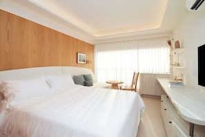 A hotel room with a large bed, a small round table, a chair, a desk with a computer, and a window with curtains. - MOBE Studios (São Paulo)