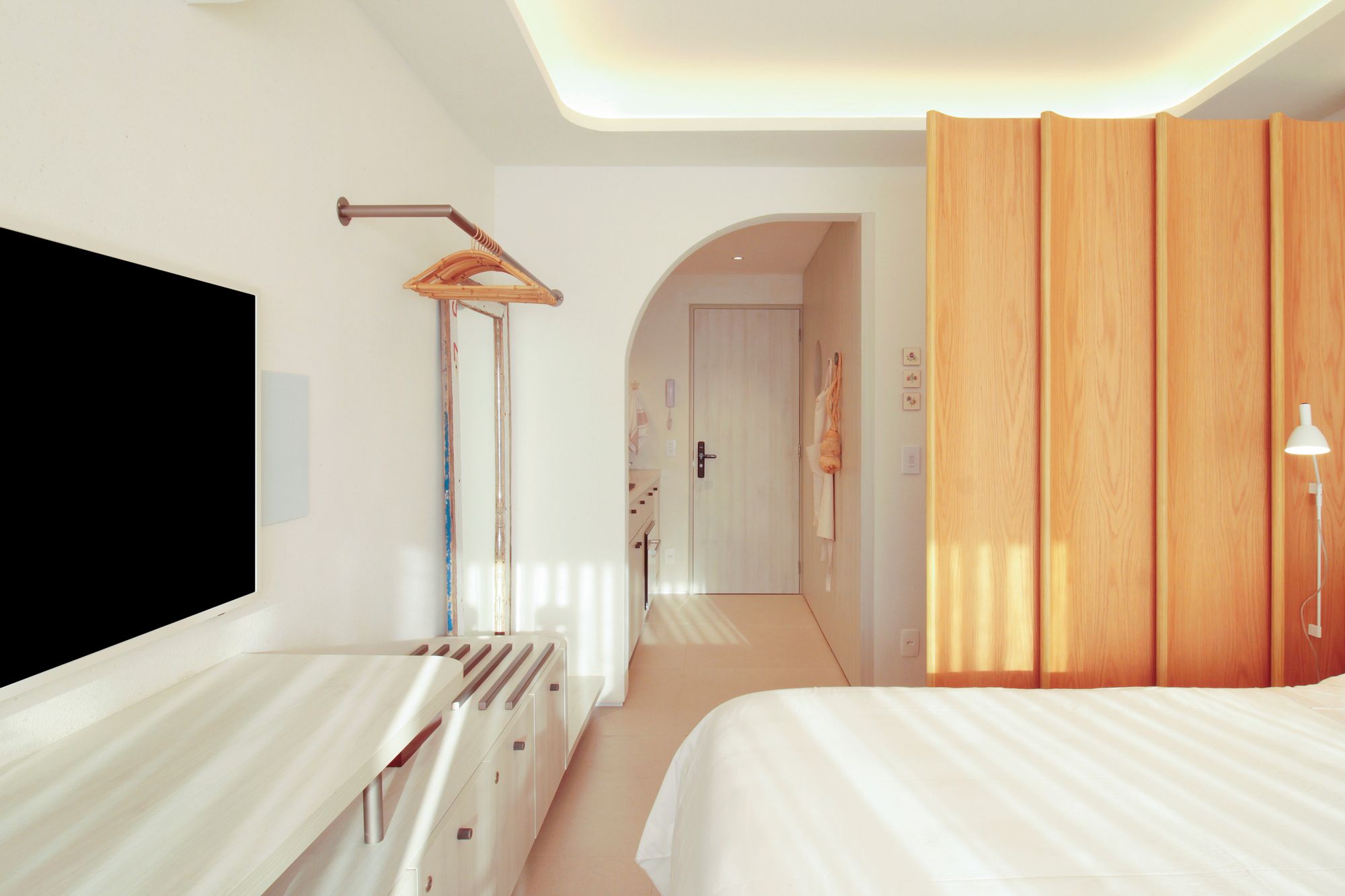 A hotel room with a bed, a desk, a TV, and a wooden partition.