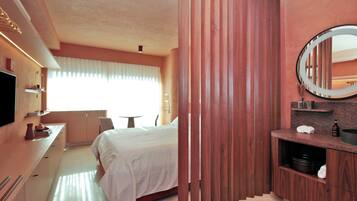 Habitación de hotel con cama, mesita de noche, espejo y vistas al exterior.