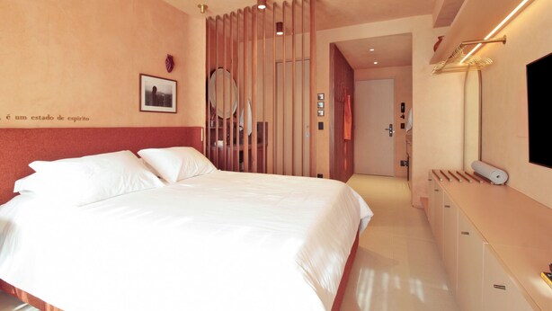 Habitación de hotel con una cama, un tocador, un espejo y una puerta que da a otra habitación.