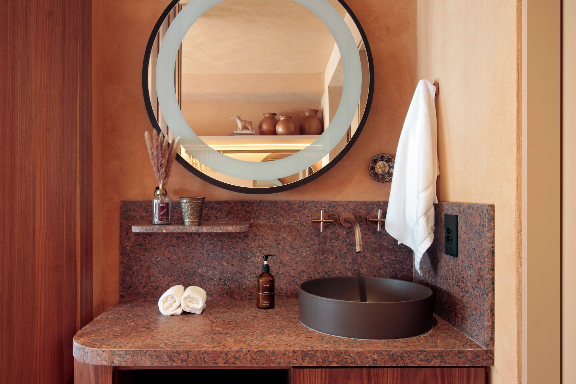 A bathroom with a round mirror, a sink, and a towel rack.